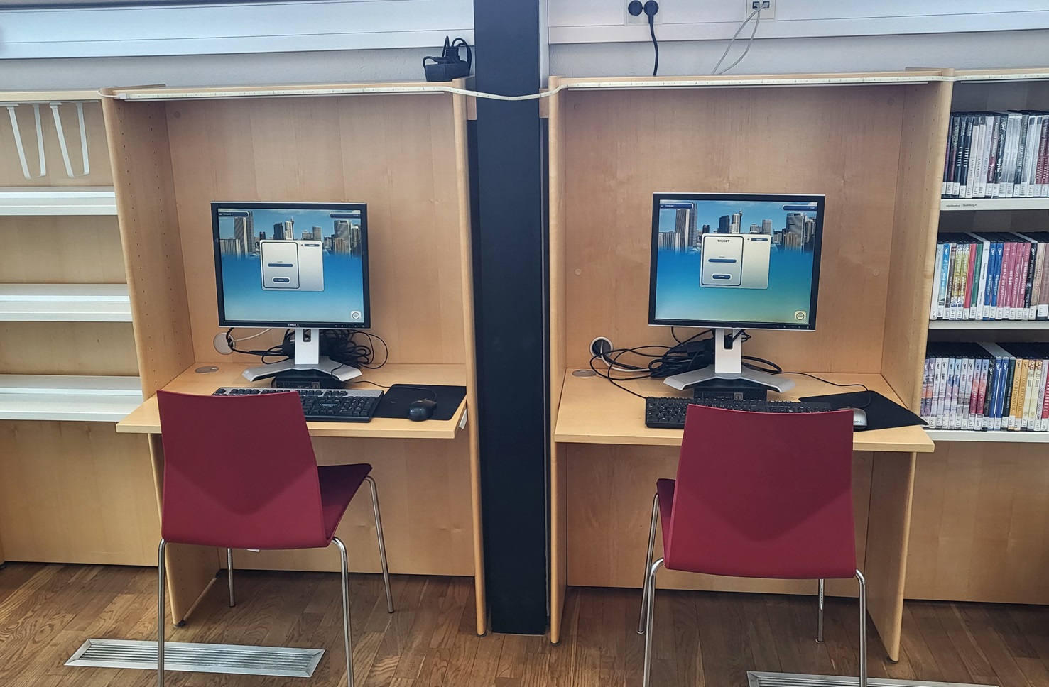 Two computers on desks in between bookshelves