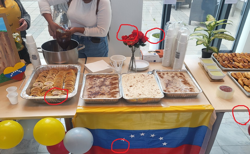 Food in trays and pot on a table with the Venezuelan flag in front