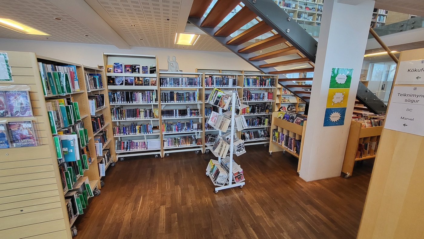Books in shelves, book stand and a view of stairs leading up