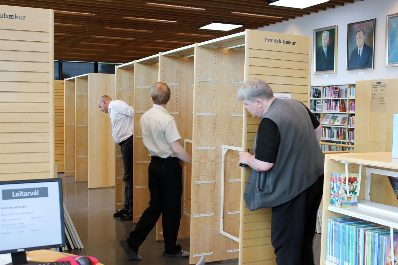 Three male employees of the library put together and move bookshelves